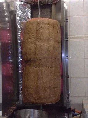 Pystysuora donerkebab-varras paistumassa: suuri lihapotkuri aluminin ja ruostumattoman teraksen valissa.