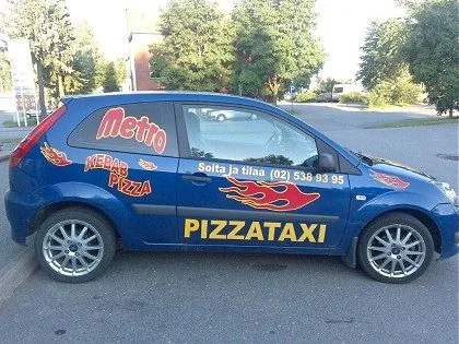 Metro Kebab -pizzataksi: sininen Ford Fiesta, tulitarrat ja suuret keltaiset PIZZATAXI-kirjaimet.