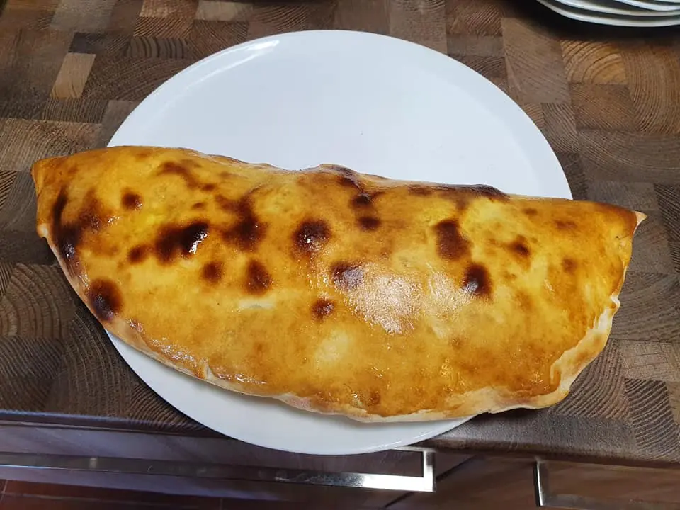 Puolikuun muotoinen calzone valkoisella lautasella, kultaruskea paistettu kuori.